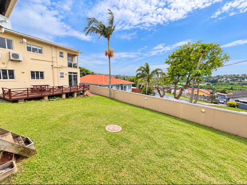 A spacious rear garden featuring a raised timber deck, perimeter boundary wall, and established landscaping with views of the surrounding neighborhood.
