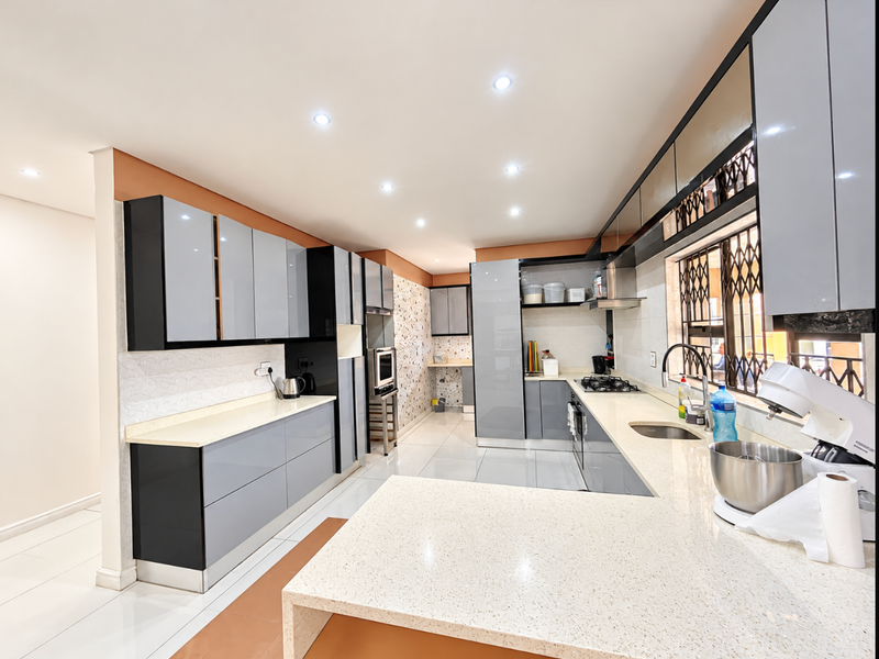 Modern kitchen featuring sleek grey cabinetry, quartz countertops, integrated appliances, and high-quality tiled flooring with ample workspace and recessed lighting.
