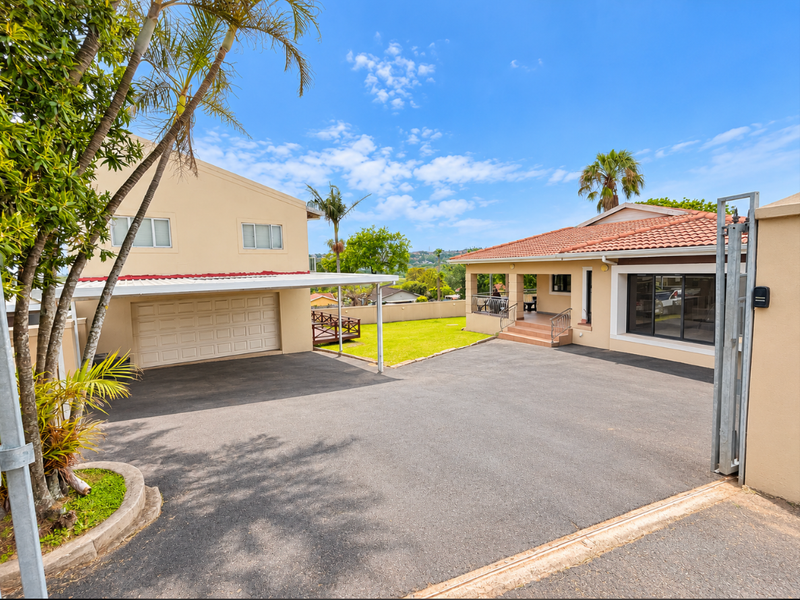 Spacious paved driveway leading to a double garage and main residence entrance with a covered patio and well-maintained exterior finishes.