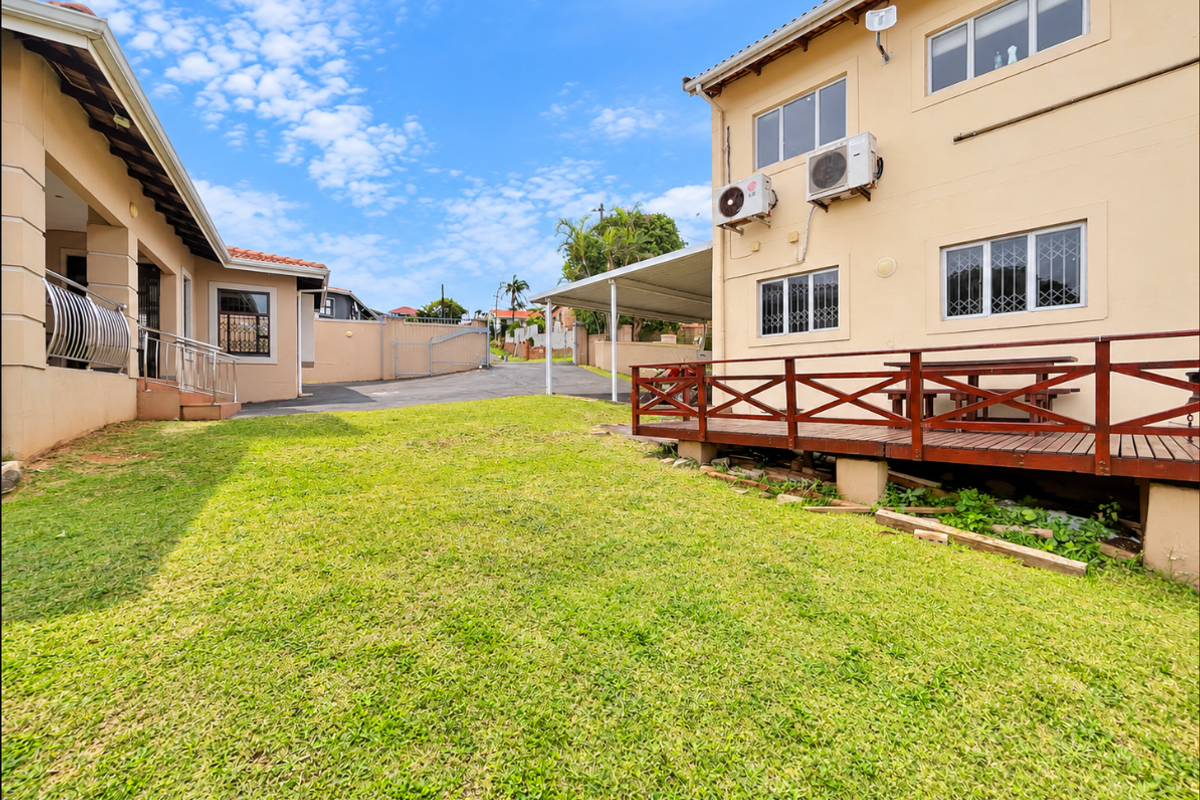 Rear exterior view featuring a lawn, a raised timber deck, and a paved driveway area with a carport.