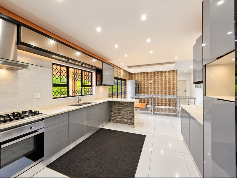 Modern kitchen featuring high-gloss cabinetry, stone countertops, integrated gas hob and oven, double sink, and sleek tiled flooring with ample recessed lighting.