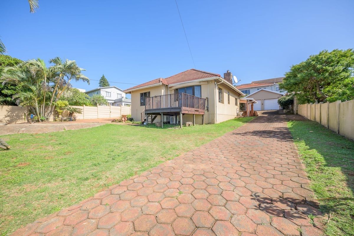 Rear view of the property featuring a raised timber deck, a large paved driveway, and a spacious garden area with boundary walling.