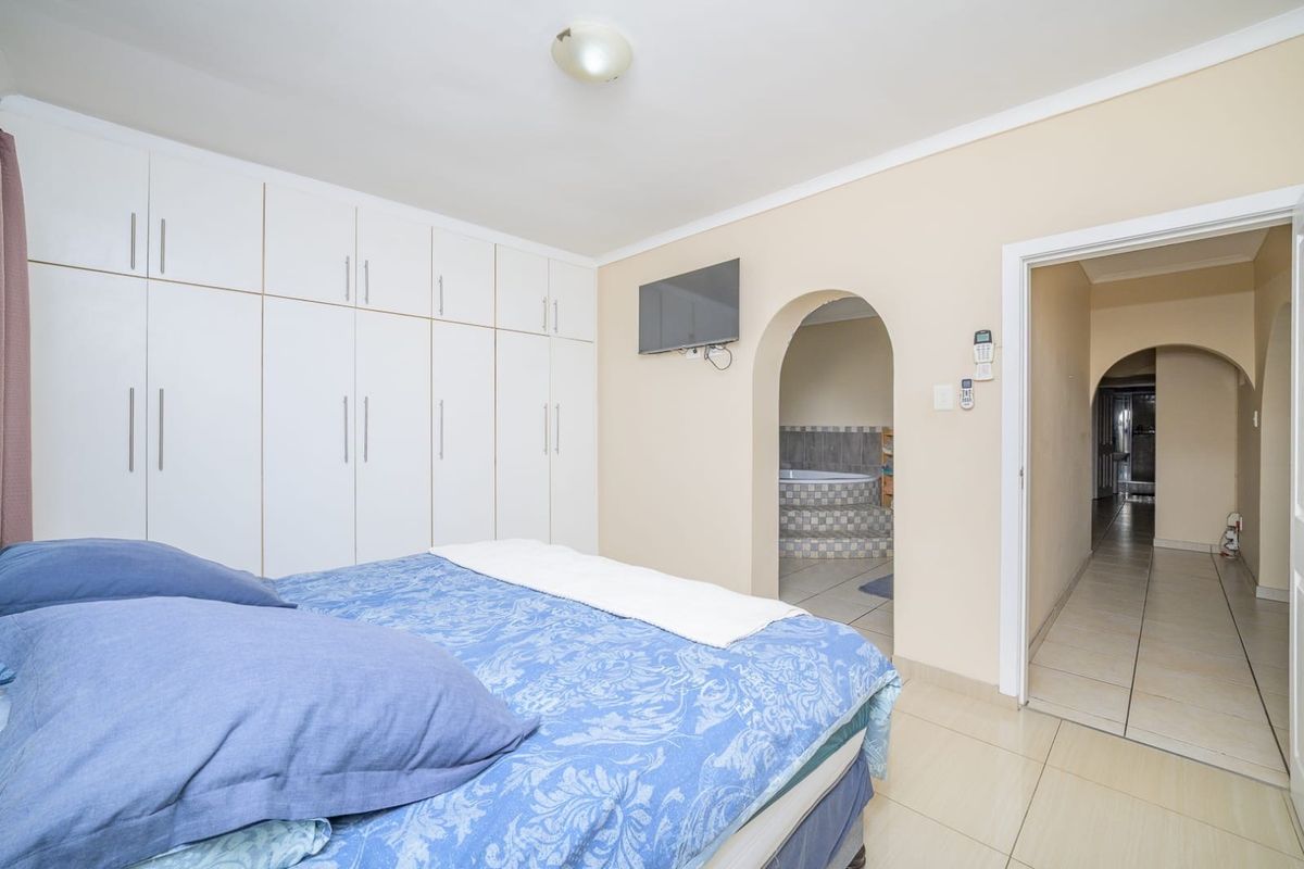 Bedroom featuring extensive built-in cupboards, tiled flooring, and an arched doorway leading to an en-suite bathroom area.