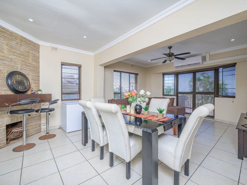 Spacious open-plan living and dining area featuring a stone accent wall, tiled flooring, ceiling fan, and split-system air conditioning with access to outdoor space.
