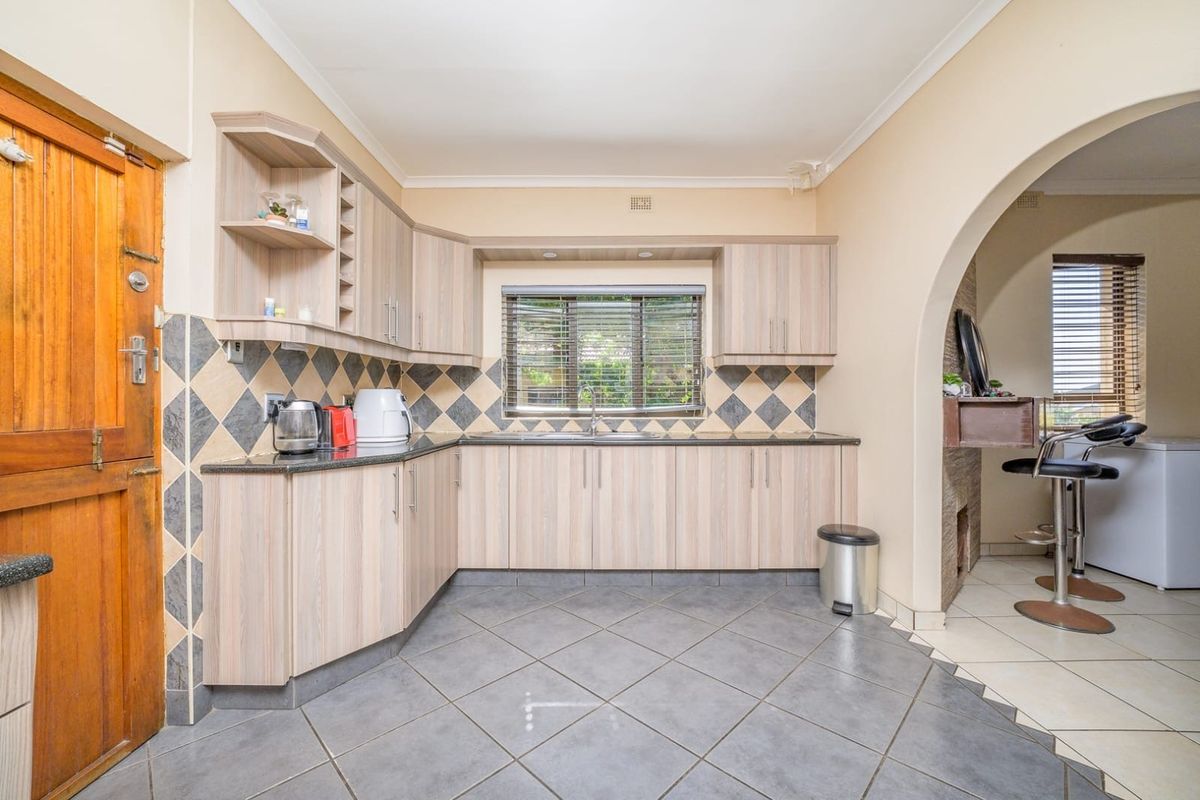 A functional kitchen featuring light wood-tone cabinetry, granite countertops, a tiled backsplash, and ceramic floor tiles, connected to an adjacent space via an archway.