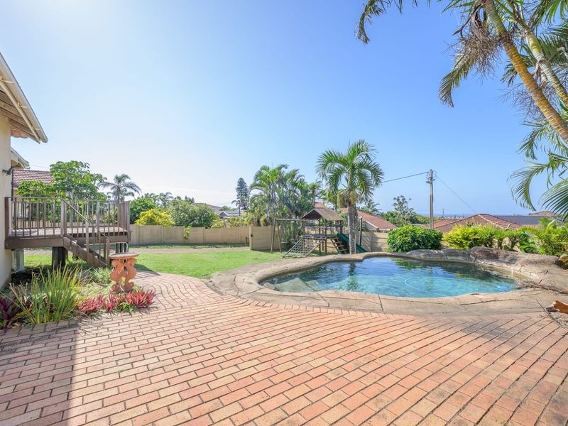 Spacious backyard featuring a swimming pool, brick-paved patio area, and a raised wooden deck, perfect for outdoor entertaining.