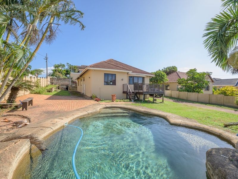 A rear garden view featuring a swimming pool, brick paved patio area, and a raised wooden deck attached to the main house structure.