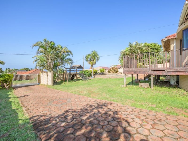 Rear exterior view featuring a paved driveway, a raised wooden deck, and a spacious garden area with perimeter fencing.