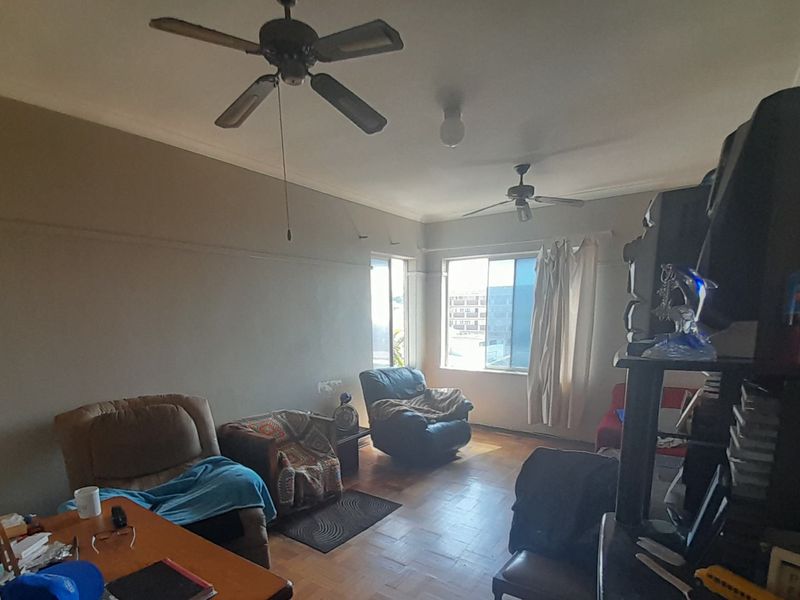 A living room featuring parquet flooring, dual ceiling fans, and large windows providing natural light.