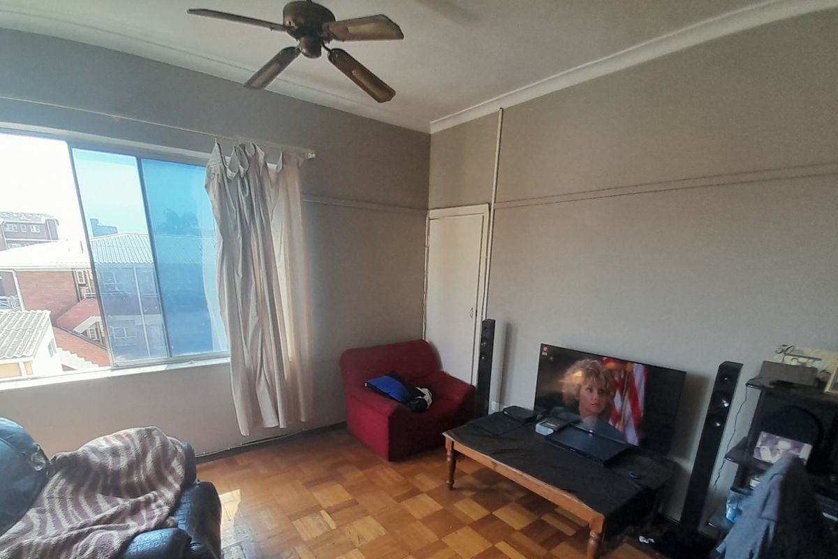 A living room featuring original parquet flooring, a ceiling fan, and a large sliding window with natural light.
