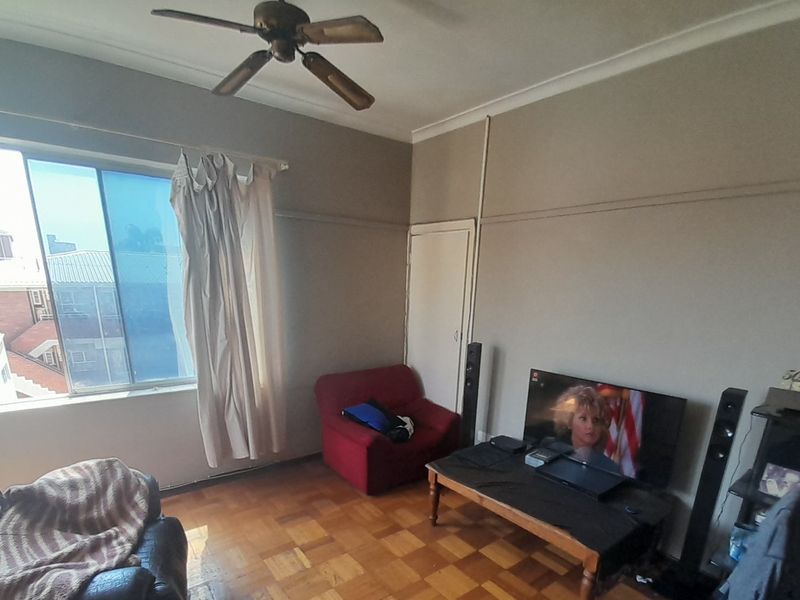 A living room featuring original parquet flooring, a ceiling fan, and a large sliding window with natural light.
