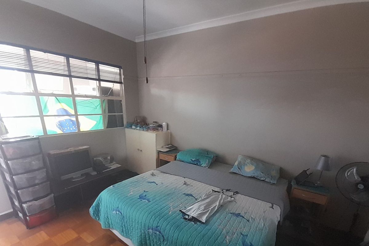 A bedroom featuring parquet flooring and a large multi-pane window, providing natural light and a functional layout.