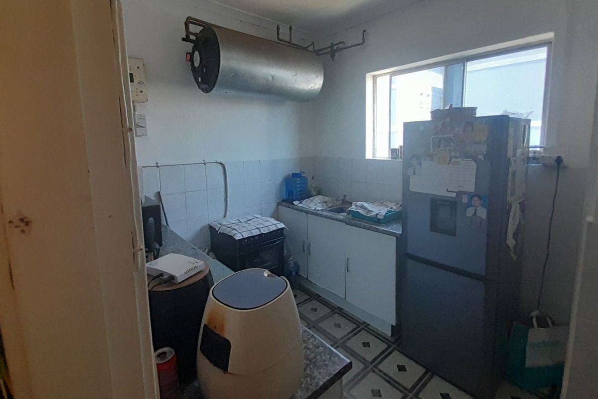 A compact kitchen featuring basic cabinetry, a sink, and an exposed wall-mounted electric geyser, requiring modernization to improve functionality and aesthetic appeal.