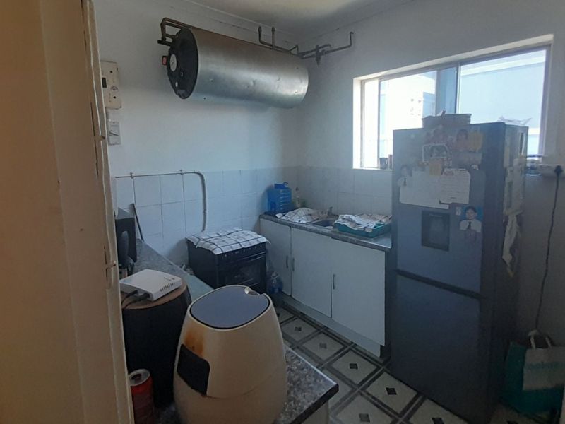 A compact kitchen featuring basic cabinetry, a sink, and an exposed wall-mounted electric geyser, requiring modernization to improve functionality and aesthetic appeal.
