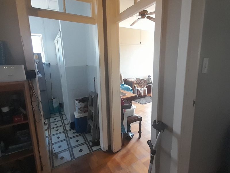 A view from a hallway looking into a kitchen area and an adjacent room, featuring a mix of tiled and parquet flooring.