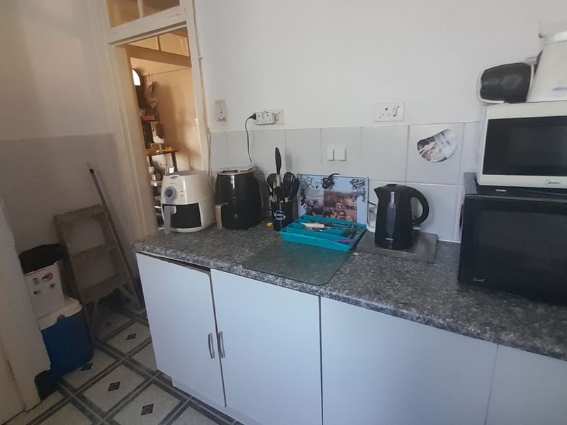A compact kitchen area featuring laminate countertops, tiled backsplash, and base cabinetry, requiring cosmetic updates to modernize the space.