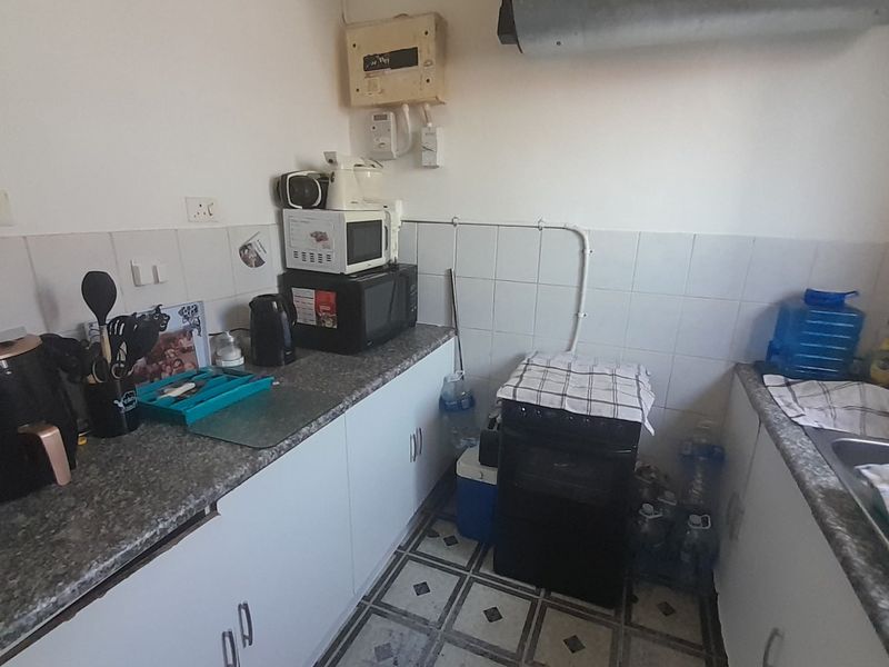 A compact kitchen featuring laminate countertops, tiled backsplash, built-in cabinetry, and a stainless steel sink, requiring cosmetic updates to improve functionality and aesthetic appeal.