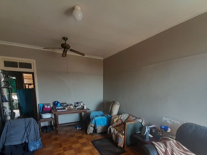 A living room featuring original parquet flooring, a ceiling fan, and coved cornicing, requiring some cosmetic wall repairs.