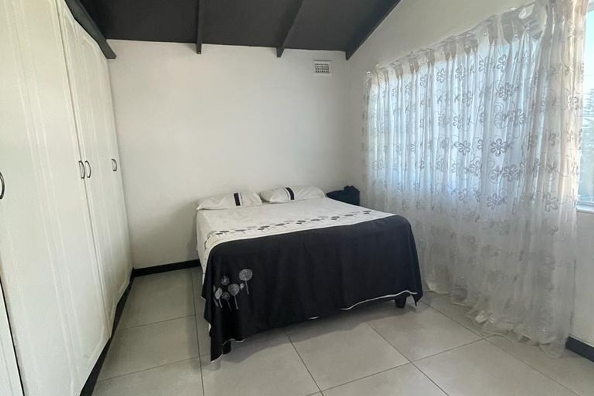 A bedroom featuring tiled flooring, built-in cupboards, and an exposed beam ceiling, offering a functional and neutral living space.