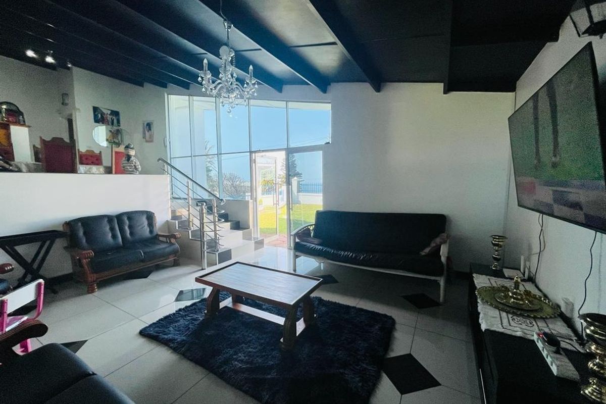 Spacious living room featuring exposed ceiling beams, tiled flooring, and large glass windows providing natural light and access to the outdoor area.