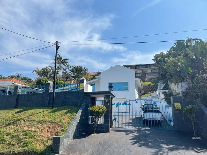 Front elevation of the property featuring a paved driveway, secure gated entrance, and tiled boundary walling.