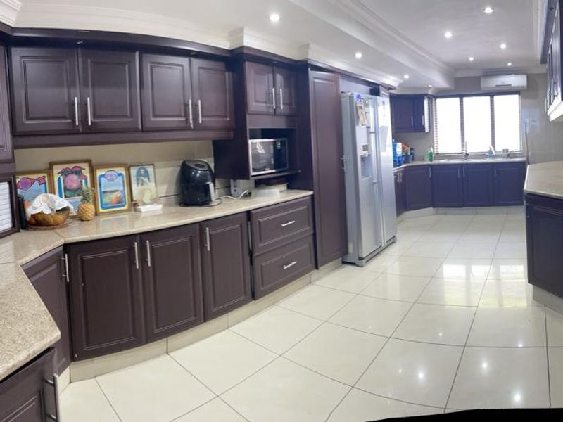 Spacious kitchen featuring dark wood cabinetry, stone countertops, tiled flooring, and integrated appliances, offering a functional and well-lit culinary workspace.