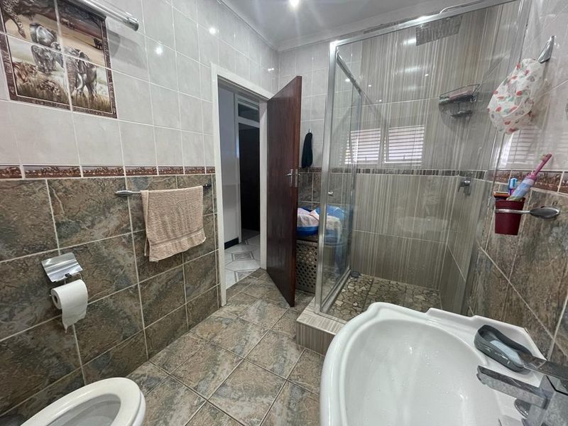 A functional bathroom featuring a glass-enclosed shower, tiled walls and flooring, a pedestal basin, and a toilet.