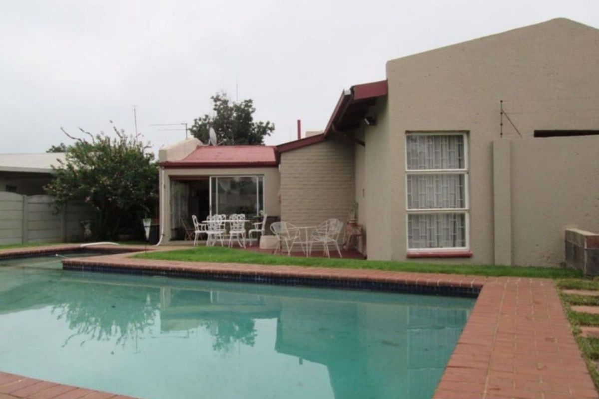Rear view of the property featuring a swimming pool with brick coping, sliding door access to the interior, and a metal roof.