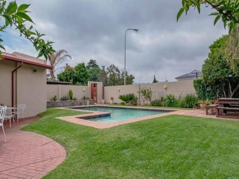 A private backyard featuring a swimming pool, surrounding lawn, and brick-paved patio area enclosed by a perimeter wall.