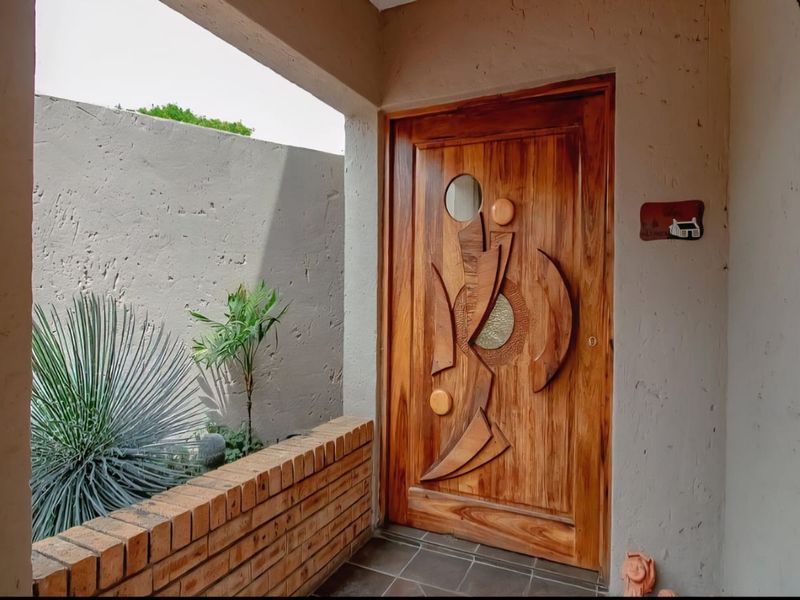 A welcoming entrance featuring a unique, custom-crafted wooden front door, complemented by a brick planter box and neutral plastered walls.