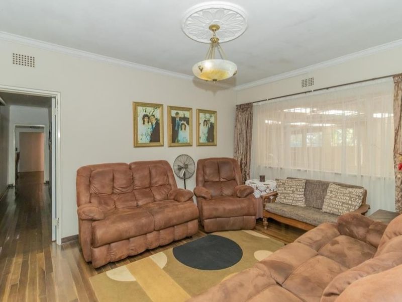 A traditional living room featuring hardwood flooring, a decorative ceiling rose, and coved cornicing, offering a dated aesthetic ready for modernization.