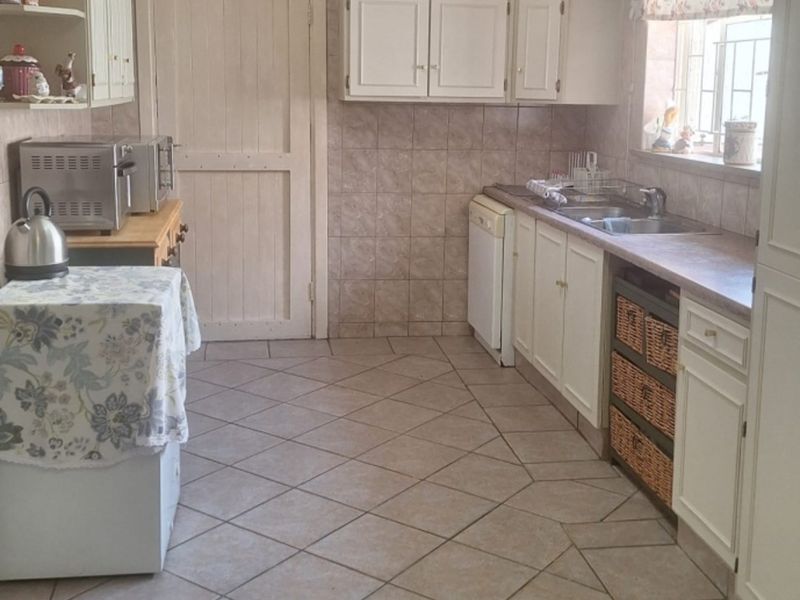 A functional kitchen featuring tiled walls and flooring, built-in cabinetry, laminate countertops, and a stainless steel sink.