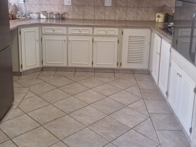 A functional kitchen featuring neutral cabinetry, tiled backsplash, and durable floor tiles, offering a classic layout with integrated oven and ample counter space.