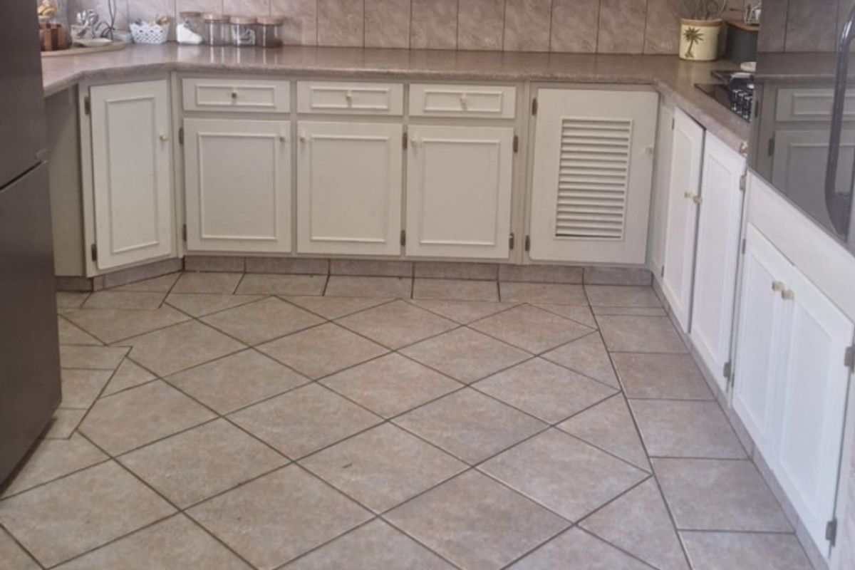 A functional kitchen featuring neutral cabinetry, tiled backsplash, and durable floor tiles, offering a classic layout with integrated oven and ample counter space.