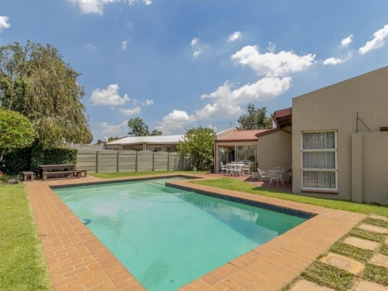 A private backyard featuring a swimming pool with brick paving, a well-maintained lawn, and direct access to the home via a sliding door.