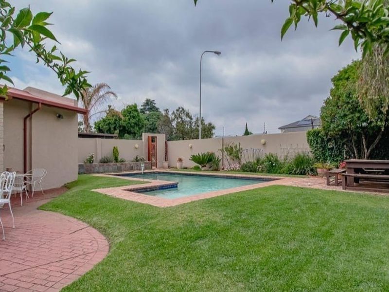 A private backyard featuring a swimming pool, paved patio area, and well-maintained lawn enclosed by a perimeter wall.