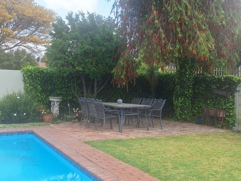 A private outdoor pool area featuring a brick-paved patio, well-maintained lawn, and established garden surroundings, ideal for outdoor relaxation and entertainment.