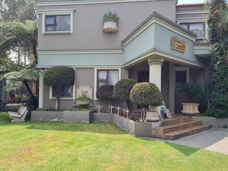 Front elevation of a two-story house featuring a covered entrance porch, paved driveway, and landscaped garden beds with a decorative stone fountain.
