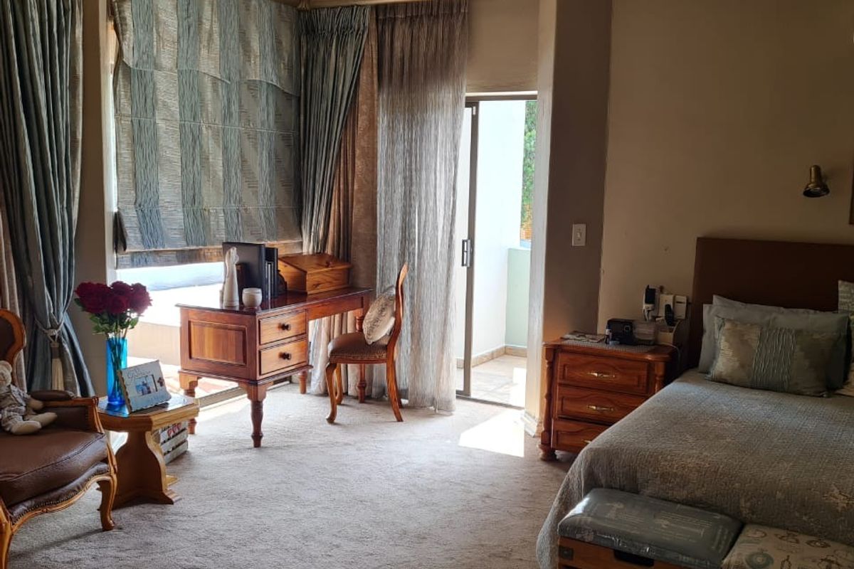 A well-maintained bedroom featuring carpeted flooring, a sliding glass door leading to a balcony, and classic wall-mounted lighting.