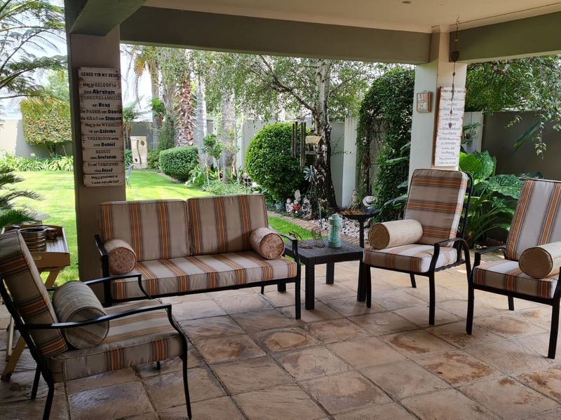 A covered outdoor patio area featuring tiled flooring and recessed ceiling lighting, overlooking a landscaped garden.