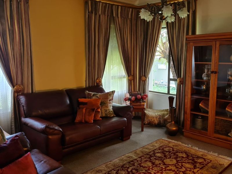 A traditional living room featuring a bay window with floor-to-ceiling curtains, carpeted flooring, and decorative ceiling cornicing.
