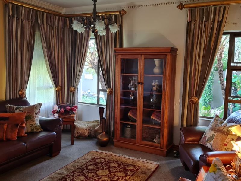 A traditional living room featuring large windows with heavy drapery, carpeted flooring, and decorative ceiling cornicing.