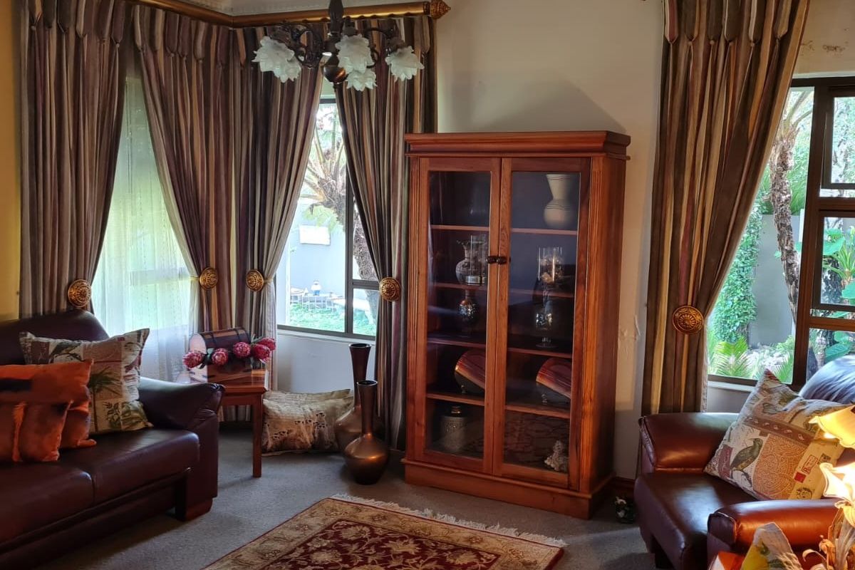A traditional living room featuring large windows with heavy drapery, carpeted flooring, and decorative ceiling cornicing.