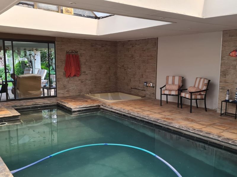 Indoor swimming pool area featuring a sunken spa bath, large skylight for natural light, and tiled finishes with direct access to the patio.