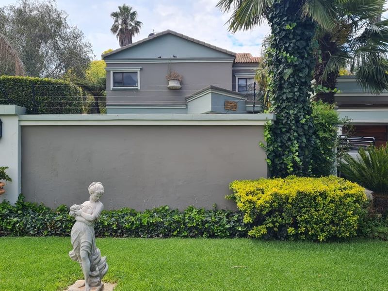 A view of the rear elevation of the house featuring a well-maintained garden, perimeter wall with electric fencing, and established landscaping.