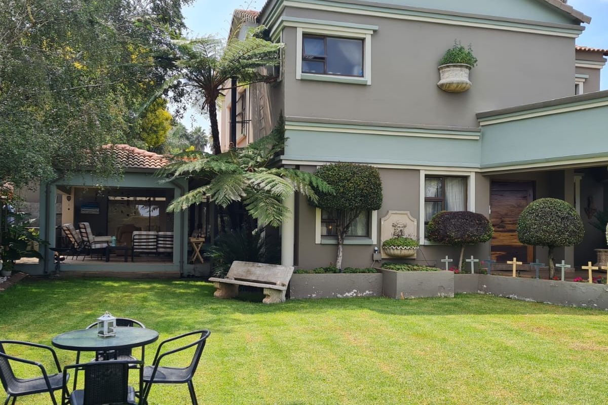Rear view of a two-story house featuring a covered patio, landscaped garden, built-in wall fountain, and raised garden beds.