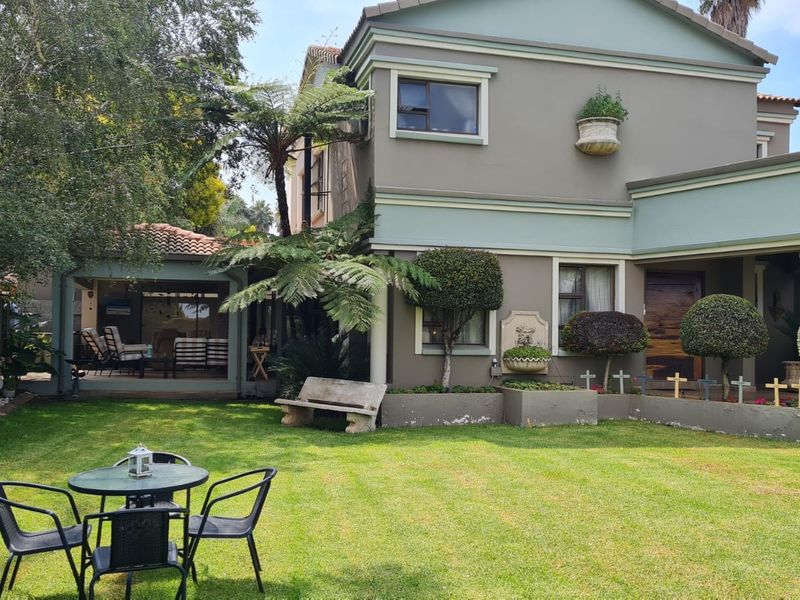 Rear view of a two-story house featuring a covered patio, landscaped garden, built-in wall fountain, and raised garden beds.