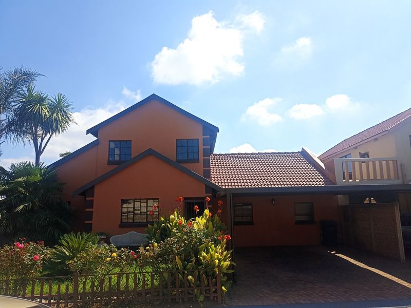 Front view of a two-story residential house featuring a tiled roof, attached carport, paved driveway, and a small balcony.