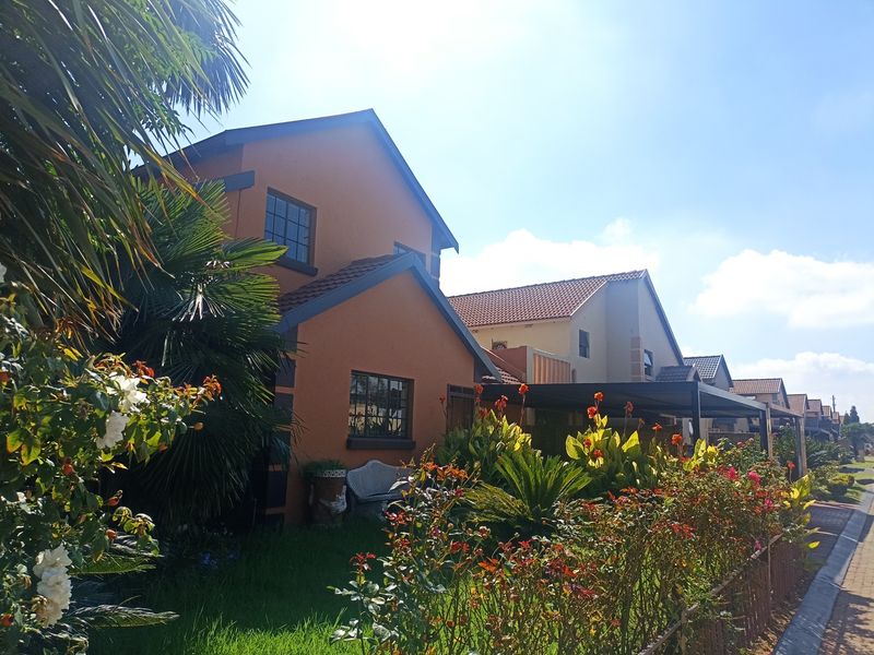 A well-maintained residential property featuring a terracotta facade, tiled roof, and a landscaped front garden with a paved driveway.