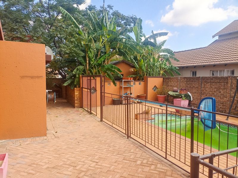 Outdoor pool area featuring brick paving, metal safety fencing, and a brick boundary wall, set within a private backyard space.